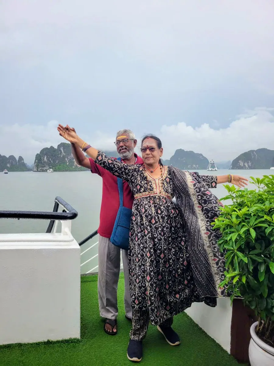 A couple with their arms spread on the sun deck of a Halong Bay cruise boat, limestone karsts behind them