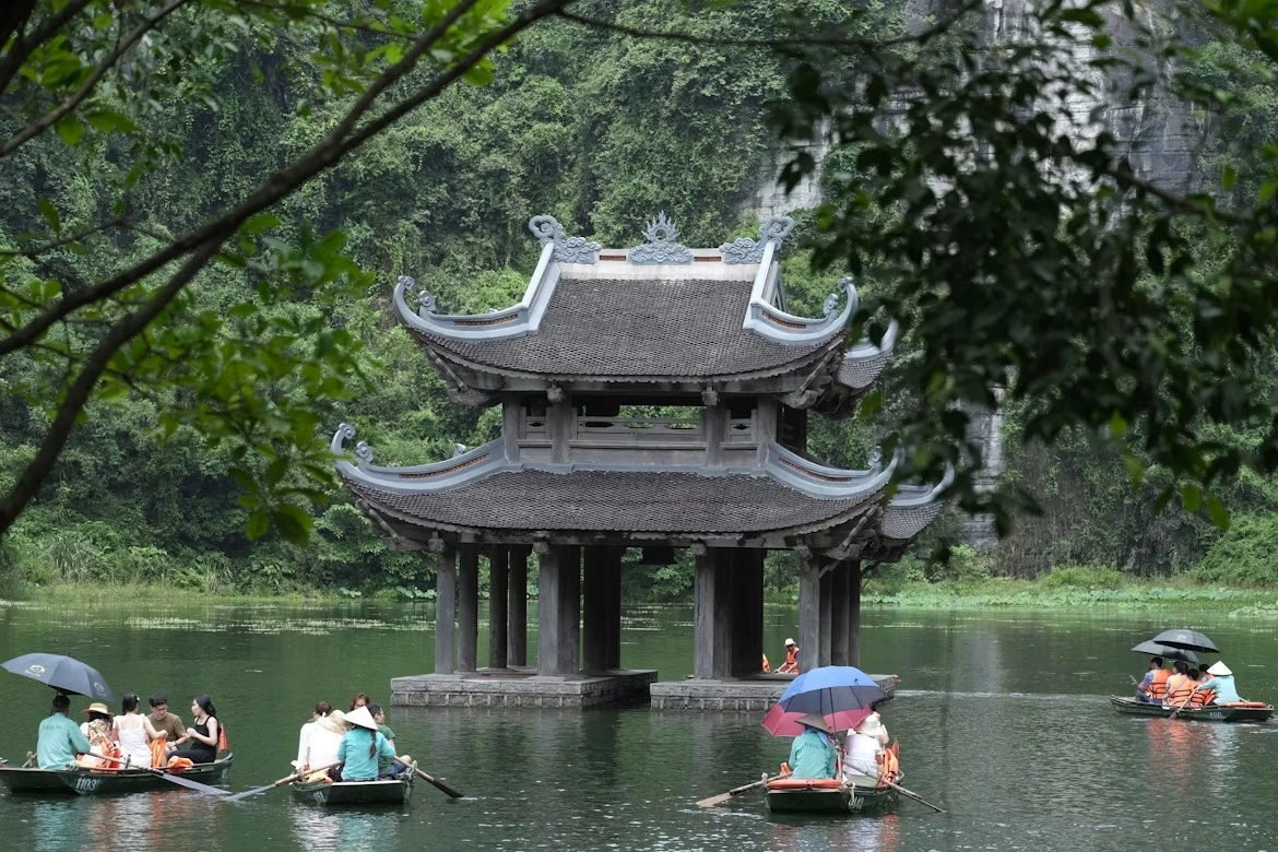 Sampans passing a temple pavilion on the river beneath the karst cliffs of Trang An, Ninh Binh
